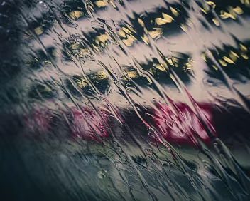 Distant Glow Rain-covered train window with blurred city lights in red and yellow shining through streaked water.