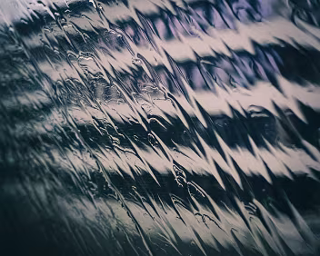 Holding Pattern Close-up of rain running diagonally across a train window, creating repeating streaks over a softly blurred urban background.