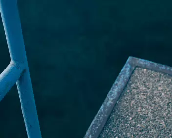 Edge A railing cuts diagonally across the frame, separating solid structure from open water. The image holds the viewer at the boundary, unresolved and slightly off...