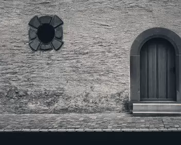 Arched Entry Rough stone wall with arched wooden door and small circular window.