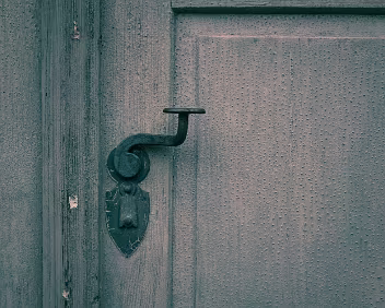 Handled Time A worn door knob set against peeling paint, marked by repeated touch. The surface records routine contact, where function slowly reshapes material.