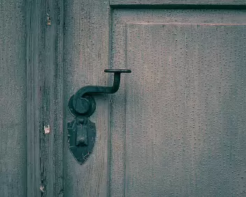 Handled Time A worn door knob set against peeling paint, marked by repeated touch. The surface records routine contact, where function slowly reshapes material.