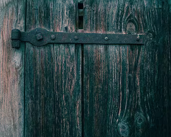 Load Bearing A corroded hinge anchors aged wood, carrying weight long after its original finish has faded. Function persists as structure absorbs time.